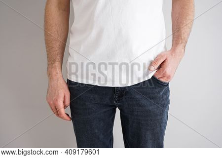 Legs Of A Young Man In Jeans With A Hand In A Pocket On Gray Background.