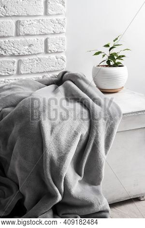 White Wooden Box With Gray Soft Fleece Blanket And Young Ficus Plant In White Flower Pot On It. Whit