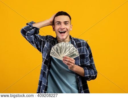 Excited Young Man Enjoying Big Jackpot, Holding Lots Of Money, Cannot Believe His Luck On Orange Stu