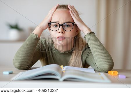 Upset Caucasian Teen Girl In Glasses Sitting At Table With Exercise Book And Touching Her Head, Doin