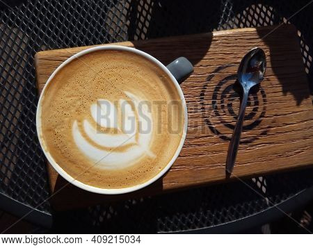 Top View Of A Cup With Cappuccino At A Cafe On A Sunny Day, Served On A Wooden Trencher On A Grid Me