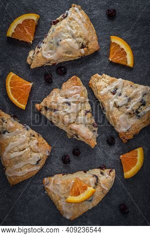 Glazed Cranberry Orange Scones On A Slate Countertop With Dried Cranberries And Orange Wedges