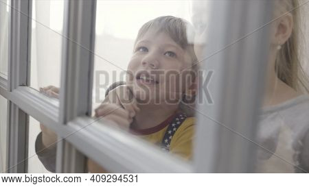 Little Children Boy And Girl Standing Behind The Door With Glass Inserts. Action. Sister And Brother
