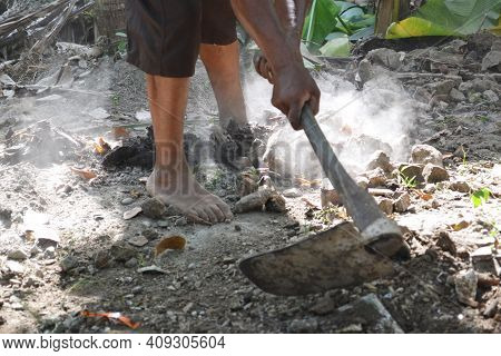 Workers' Feet And Hands Holding Hoe Stalks As Work Clearing Stones And Dirt In The Dusty Dirt Yard