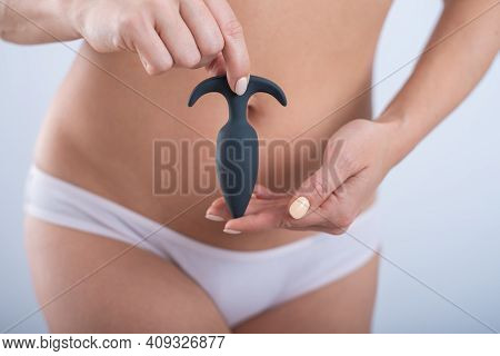 A Faceless Woman In White Cotton Panties Holds A Black Butt Plug On A White Background