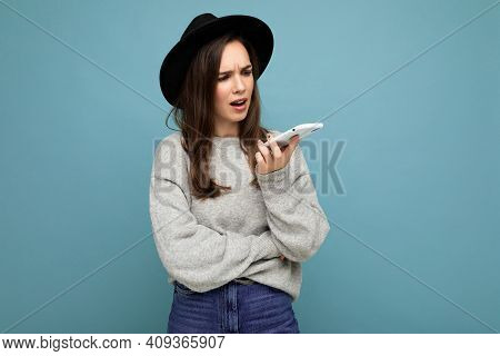 Young Asking Dissatisfied Brunette Woman Wearing Black Hat And Grey Sweater Holding Smartphone Looki