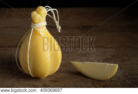 Head And Slice Of Typical Italian Cheese Caciocavallo On A Wooden Surface.