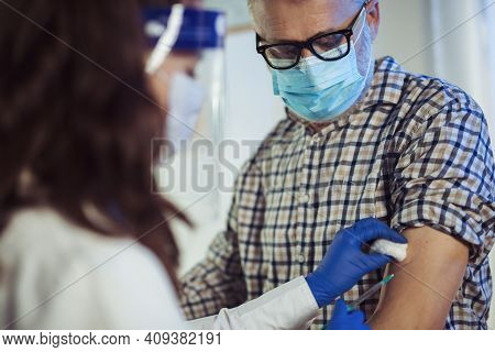 Young Woman Nurse With Surgical Mask And Face Shild Giving Injection To Senior Man. Covid-19 Or Coro