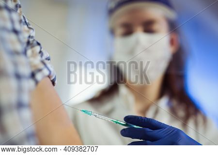 Young Woman Nurse With Surgical Mask And Face Shild Giving Injection To Senior Man. Covid-19 Or Coro