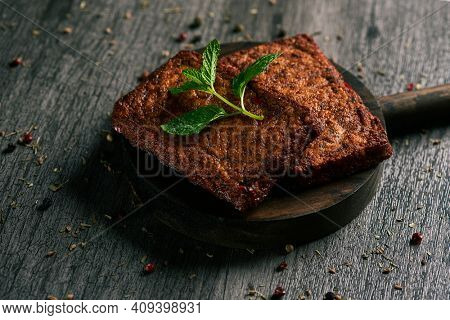 closeup of some cooked tofu fillets in a round wooden tray, on a gray wooden table