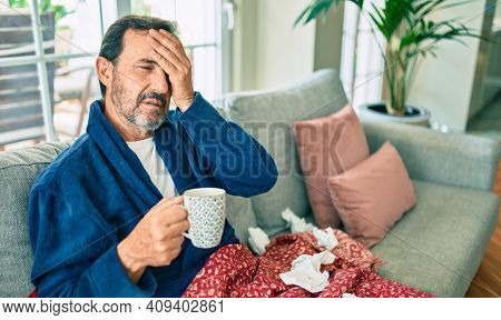 Middle age man feeling sick with cold and fever at home, ill with flu disease sitting on the sofa