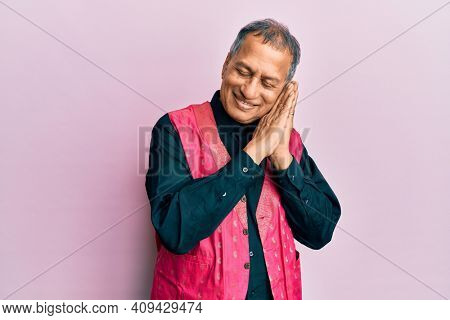 Middle age indian man wearing traditional indian clothes sleeping tired dreaming and posing with hands together while smiling with closed eyes. 