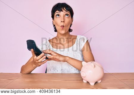 Beautiful brunettte woman caculating money savings making fish face with mouth and squinting eyes, crazy and comical. 