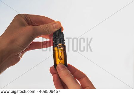 Bottle Of Cbd Or Thd Oil In Human Hand, Shot Against Blue Sky. Essential Oil, Natural Health Product