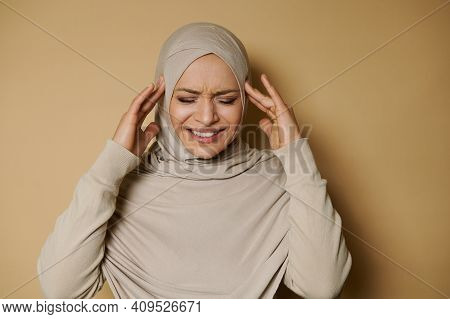 Beautiful Arab Woman In Hijab Posing To The Camera Expressing Pain And Headache On A Beige Backgroun