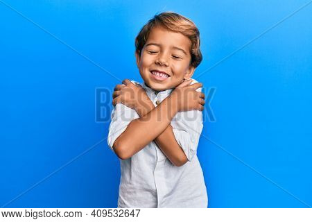 Adorable latin kid wearing casual clothes hugging oneself happy and positive, smiling confident. self love and self care 