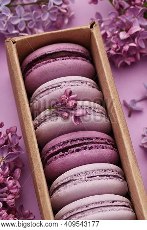 Set Of Violet And Lilac Macarons In Cardboard Gift Box With Lilac Flowers On Violet Background. Clos