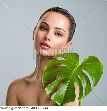 Young beautiful woman with green leave near face and body. Skin care beauty treatments concept.  Closeup girl's face with green leave. White model with clean, health skin of face - posing at studio