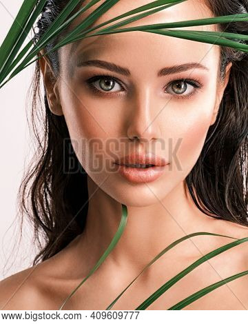 Young beautiful woman with green leaves near face and body. Skin care beauty treatments concept.  Closeup girl's face with green leave. White model with clean, health skin of face - posing at studio