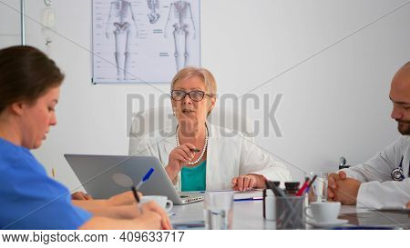 Senior Surgeon Explaining Treatment To Coworkers Presenting Plan During Medical Conference Sitting A