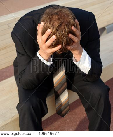 Desperate Businessman Sits Sadly On A Bank His Hands Folded Over His Head