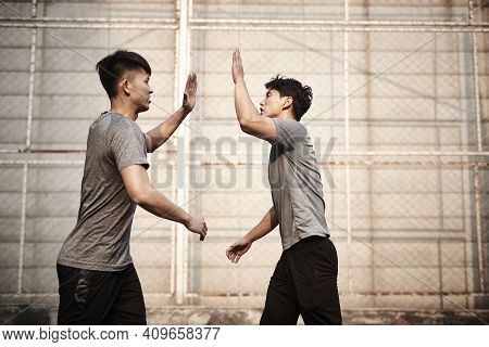 Two Young Asian Athletes Giving Hi-five Celebrating Success