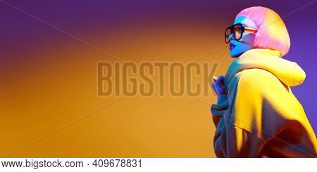 Beauty trends. Attractive fashion model girl with bright makeup and pink hair poses in modern sunglasses and yellow suit in mixed color light. Sport chic fashion. Copy space.