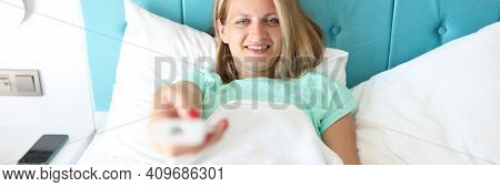 Young Woman In Bed Of Hotel Room Holds Remote Control In Hand. Remote Control Of The Quality Of Clim