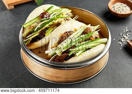 Bao bun with roast duck. Bamboo steamer on dark slate table. Chinese, asian, authentic food concept.