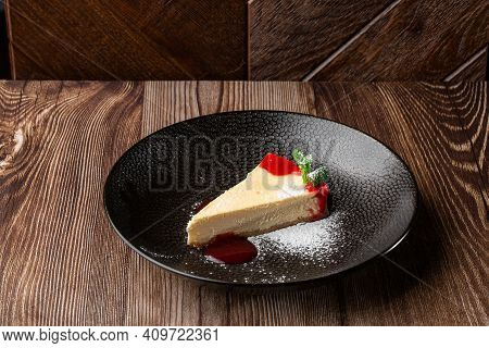 A Piece Of Cheesecake Served With Red Berry Sauce, Mint Leaf And Sugar Powder. Isolated Dish In A Bl