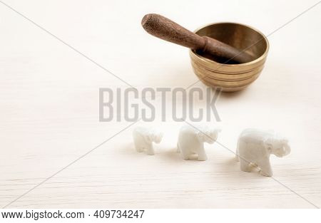 Three Elephantes Made Of Stone And Singing Bowl On White Wooden Background. Meditation And Relaxatio