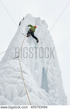 Alpinist Man With Ice Tools Axe In Orange Helmet Climbing A Lar