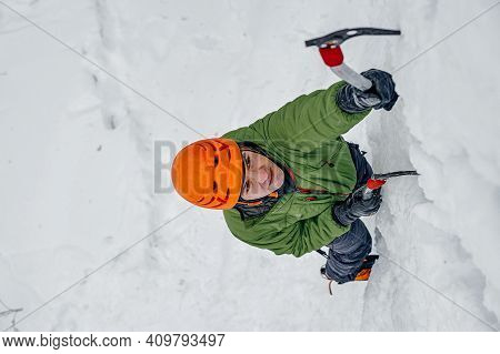 Alpinist Man With Ice Tools Axe In Orange Helmet Climbing A Lar