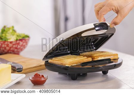 Hand Carefully Opening A Sandwich Maker With Hot Sandwiches
