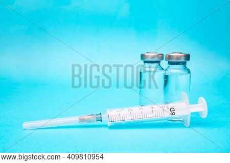 Two Ampoules Of Vaccine With A Syringe On A Blue Background. Vaccination Pictures.