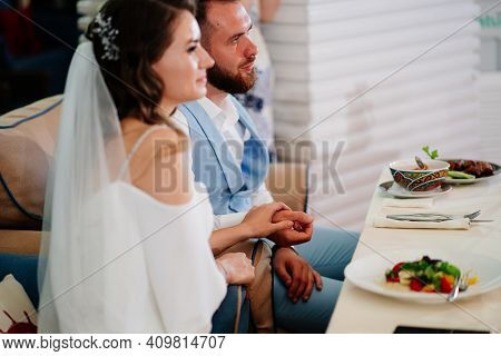 Newlyweds Sit At Table In Restaurant And Listen To Congratulations From Guests.