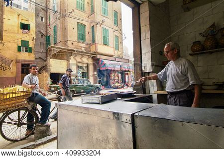 05-29-2007  Alexandria , Egypt.  Cook cooking some  fried  vegetable ball in oil  in street cafe. Some people watching on photographer