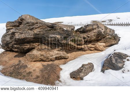 Fenced Stone Rock In The Middle Of Snowy Mountains In Winter Against A Blue Sky