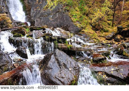 A Small Stream Flows Down From The Mountain, Bending Around The Fallen Trees And Large Stone Boulder