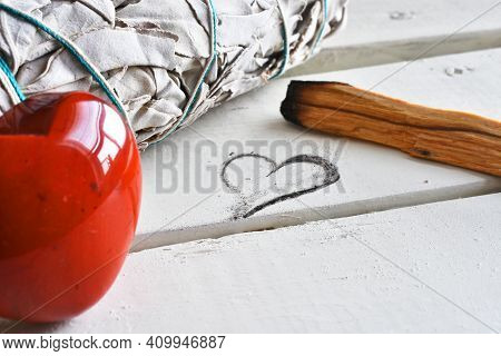 A Close Up Image Of White Sage And Holly Wood Smudge Sticks Next To A Heart Shaped Drawing.
