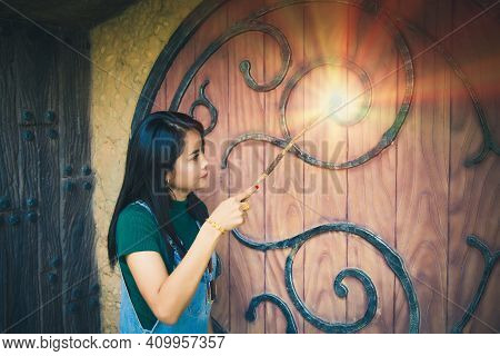 An Asian Woman Wearing In Demin Overalls Standing And Casting A Spell At A Wooden Door.