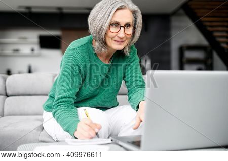 Lively Aged Woman Grey Haired Busy As A Bee, Stylishly Dressed, Sitting At The Laptop, Loft Style Ap
