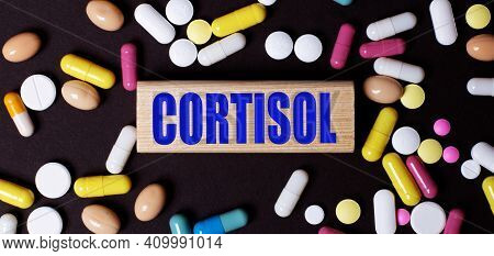 On A Dark Background, Multi-colored Pills And The Word Cortisol On A Wooden Block. Medical Concept