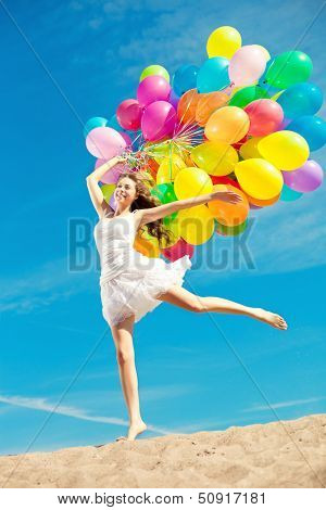 Beautiful young stylish woman with ainbow balloons in hands against the sky. Positive girl on nature. Smiling woman outdoors enjoying.