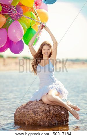 Beautiful young stylish woman with ainbow balloons in hands against the sky. Positive girl on nature. Smiling woman outdoors enjoying.