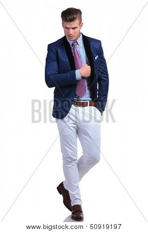 full length picture of a young business man walking toward the camera with a hand in his pocket and the other inserted in his jacket while looking away from the camera. on a white background
