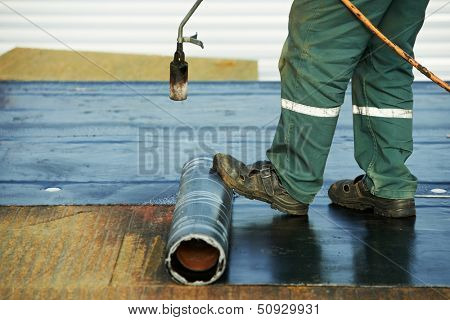 Roofer installing Roofing felt with heating and melting of bitumen roll by torch on flame during roof repair