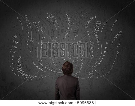 Thoughtful young businessman standing and deciding in front of a chalkboard with sketched arrows and lines in different directions