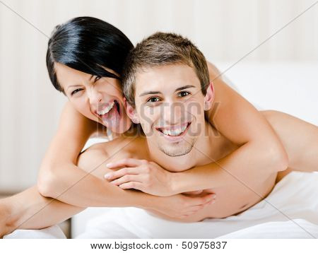 Close up of laughing couple who plays in bedroom. Woman lying on the back of the man embraces him