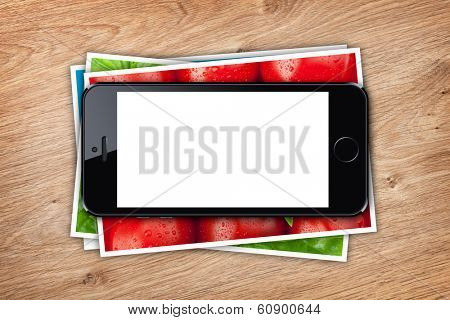 Phone with blank screen over stack of printed pictures collage on wooden table